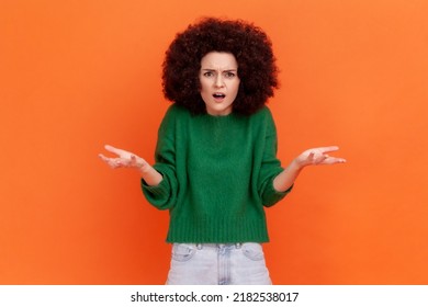 What do you want? Woman with Afro hairstyle wearing green casual sweater asking who why make this conflict, looking with annoyed indignant expression. Indoor studio shot isolated on orange background.