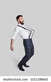 What Is Happening? Full Length Of Surprised Young Man In Suspenders Pulled By Something While Standing Against Grey Background