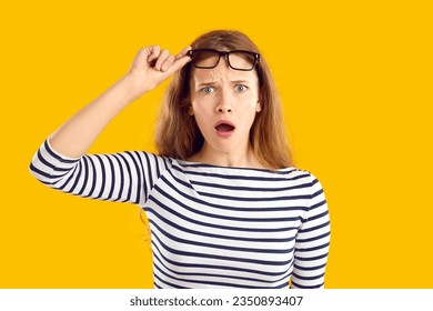 What the hell are you doing. Beautiful young woman sees something strange, lifts her eyeglasses in disbelief and looks at the camera with an open mouth and a funny, confused, shocked face expression