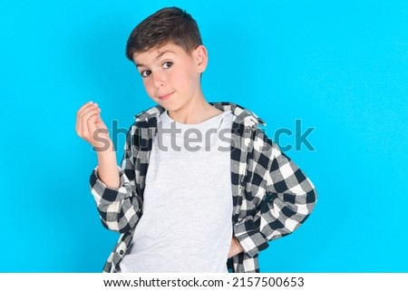 What the hell are you talking about. Shot of frustrated caucasian kid boy wearing plaid shirt over blue background gesturing with raised hand doing Italian gesture, frowning, being displeased