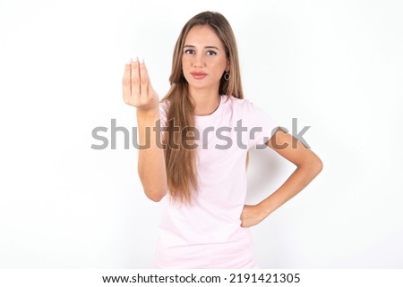 What the hell are you talking about. Shot of frustrated young beautiful woman wearing pink T-shirt over white background  gesturing with raised hand doing Italian gesture, frowning, being displeased 