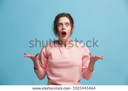What is it. The female portrait isolated on blue studio backgroud. Anger. The young emotional angry, scared woman looking at camera.The human emotions, facial expression concept. Trendy colors