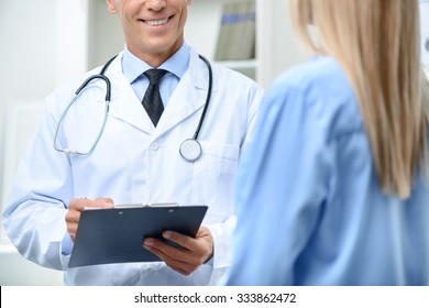 What pains. Close up of professional upbeat doctor holding folder and talking with the patient while being busy at work