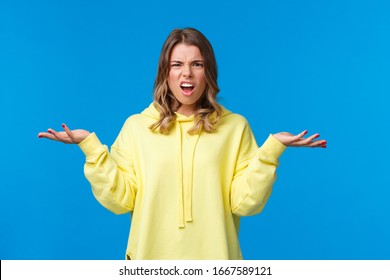 What problem wtf. Pissed-off frustrated and angry young blond caucasian girl shrugging with confused annoyed expression, cant understand what happened, dont know anything, blue background