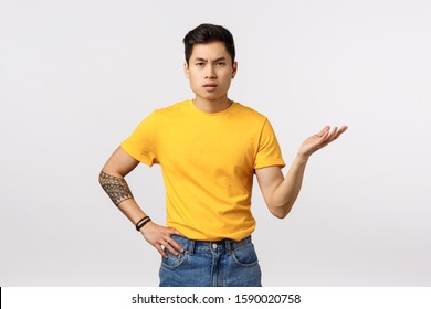 So what. Skeptical and pissed, frustrated young asian guy dont understand whats big deal, why so fuss, raising arm in dismay, standing puzzled and bothered as arguing with friend, white background