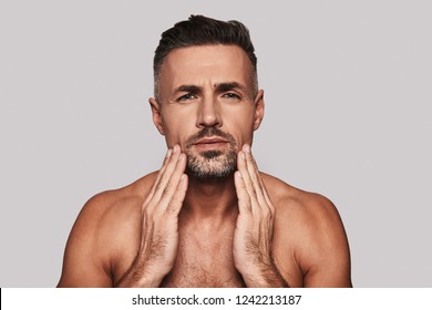 What Is Wrong With My Skin? Confused Young Man Touching His Face And Looking At Camera While Standing Against Grey Background