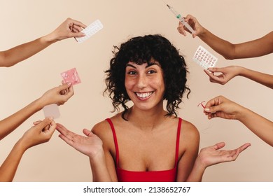 What's the contraceptive method of your choice? Happy young woman smiling at the camera while surrounded by hands holding different forms of hormonal and non-hormonal contraception. - Shutterstock ID 2138652767