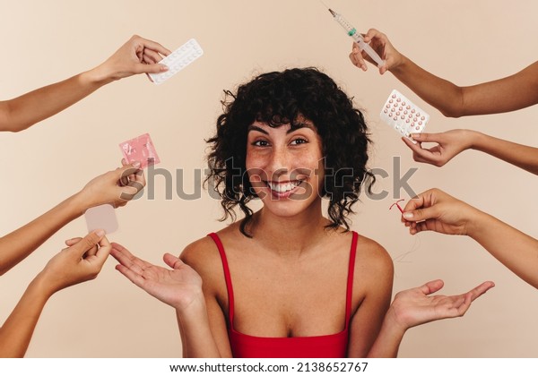What\'s the\
contraceptive method of your choice? Happy young woman smiling at\
the camera while surrounded by hands holding different forms of\
hormonal and non-hormonal\
contraception.
