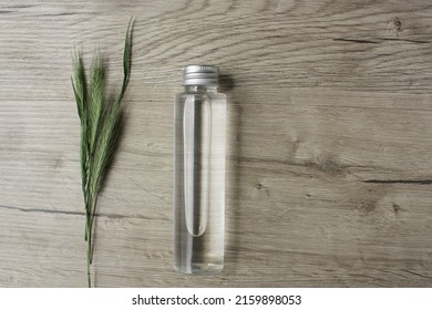 Wheat barley rye oat essence in a glass bottle and green young fresh wheat ears on wooden background with copy space. Cosmetic essence oil template ad. Bottle product with wheat rye barley