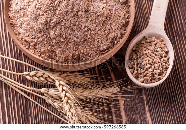Wheat bran in wooden bowl and ears of wheat on a\
wooden table
