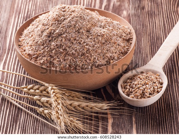 Wheat bran in wooden bowl and ears of wheat on a\
wooden table