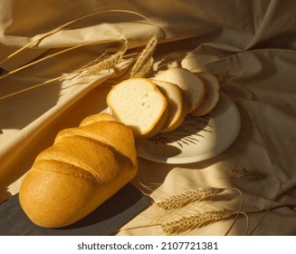 Wheat bread with golden crust and slices of bread on ceramic plate on beige cotton background. German traditional bakery and handmade tin loaf, white bread. Daily food concept. Earth tone colors.