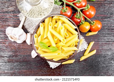 Wheat flour penne pasta in a bowl of coconut shells on sacking, tomatoes, garlic, vegetable oil in a decanter and parsley on wooden board background from above - Powered by Shutterstock