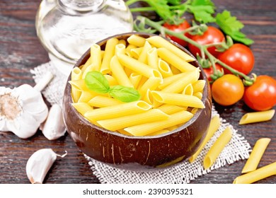 Wheat flour penne pasta in a bowl of coconut shells on sacking, tomatoes, garlic, vegetable oil in a glass decanter and parsley on a wooden board background - Powered by Shutterstock