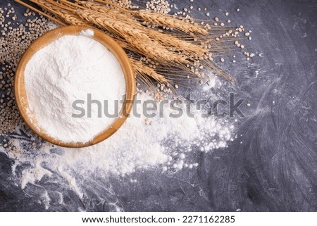Wheat flour in a wooden bowl With wheat ears on the table, black background. - top view