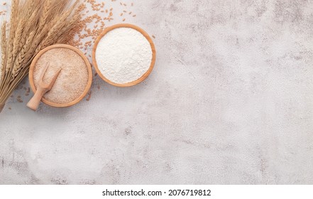 Wheat grains , brown wheat flour and white wheat flour in wooden bowl set up on white concrete background.