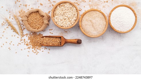Wheat grains , brown wheat flour and white wheat flour in wooden bowl set up on white concrete background. - Shutterstock ID 2248743897