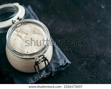 Wheat sourdough starter. Glass jar with sourdough starter on dark background, copy space.