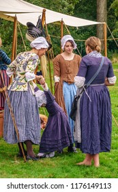 WHEATON, ILLINOIS/USA - SEPT. 8, 2018: A Girl Stretches Playfully Among Three Young Women In Period Dress At A Military Camp During A Reenactment Of The American Revolutionary War (1775-1783).