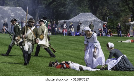 WHEATON, ILLINOIS/USA - SEPTEMBER 12, 2015: Two Young Women Nurses Attend To A Fallen Soldier While Other Combatants March By At A Reenactment Of The American Revolutionary War (1775-1783).