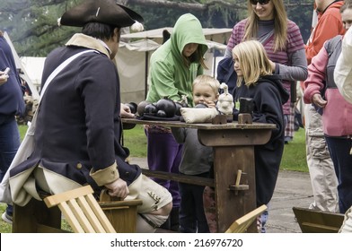 WHEATON, ILLINOIS/USA - SEPTEMBER 13, 2014: A Boy Reaches For A Cannonball On Display While Family Members And A Soldier-actor Look On During Reenactment Of The American Revolutionary War (1775-1783).