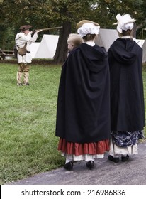 WHEATON, ILLINOIS/USA - SEPTEMBER 13, 2014: Two Women Reenactors, One Holding A Baby, Watch A Militia Member Aim His Musket During A Reenactment Of The American Revolutionary War (1775-1783).