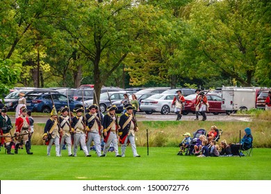 WHEATON, IL/USA - SEPT. 7, 2019: Children And Two Women Watch Soldiers With Muskets March Past Them At The End Of A Mock Battlefield During A Reenactment Of The American Revolutionary War (1775-1783).