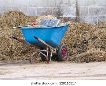 A Wheel Barrow In Front Of A Muck Heap.