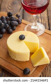 Wheel cheese and one piece and dark grapes with wine glass on cutting board,top view. - Shutterstock ID 2144154691