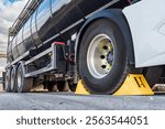 Wheel chocks placed on the drive wheel of a tanker truck to immobilize it for safety during the loading or unloading processes.