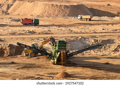 Wheel front-end loader loads sand into jaw crusher. Heavy machinery in the mining quarry, excavators and trucks. Mobile jaw crusher plant with belt conveyor puts crushing and screening process