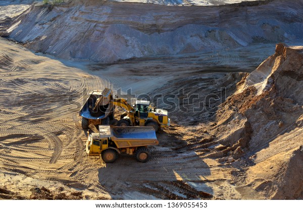 Wheel front-end loader unloading\
sand into heavy dump truck at the opencast mining\
quarry