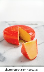 A Wheel Of Gouda Cheese Covered With Red Wax, With A Wedge Cut Out Form The Wheel