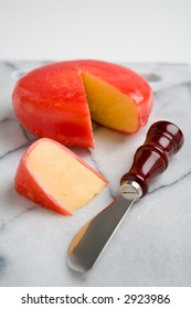 A Wheel Of Gouda Cheese Covered With Red Wax, With A Wedge Cut Out Form The Wheel