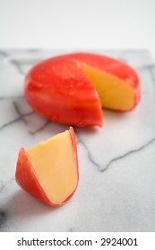 A Wheel Of Gouda Cheese Covered With Red Wax, With A Wedge Cut Out Form The Wheel