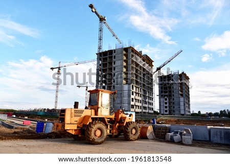 Wheel loader with a bucket at construction. Heavy machinery for loading and unloading works and road work. Public works, civil engineering, road construction. Tower crane in action. Crane on formwork
