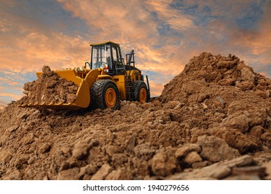 Wheel loader are digging the soil in the construction site on the  sky background after sunset