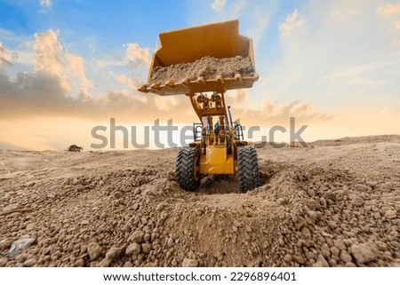 Wheel loader are digging the soil in construction site with bucket lift up on sunset background