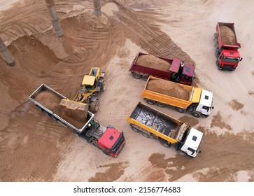 Wheel loader load sand in tipper truck in open pit. Front end loader on earthworks in open-pit mining. Heavy machinery on developing opencast. Dump truck sand transports from quarry, aerial view.