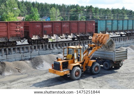 Wheel loader loads gravel into a dump truck at a cargo railway station. Fron-end loader unloads crushed stone in a gravel pit.  Unloading bulk cargo from freight cars on high railway platform Stockfoto © 