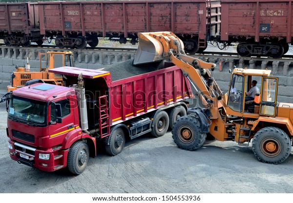 Wheel loader loads gravel into a dump truck at a\
cargo railway station. Fron-end loader unloads crushed stone in a\
gravel pit.  Unloading bulk cargo from freight cars on high railway\
platform