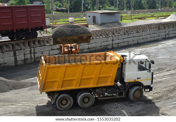 Wheel loader loads gravel into a dump truck at a\
cargo railway station. Fron-end loader unloads crushed stone in a\
gravel pit.  Unloading bulk cargo from freight cars on high railway\
platform
