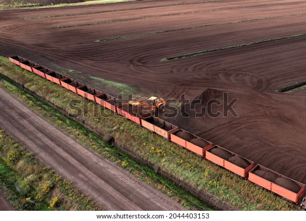 Wheel loader loads peat in freight cars.\
Aerial view of diesel locomotive on railroad in landscape at\
wetlands. Drone view of peat bog railway at peatlands. Transporting\
peat from peat\
extraction.