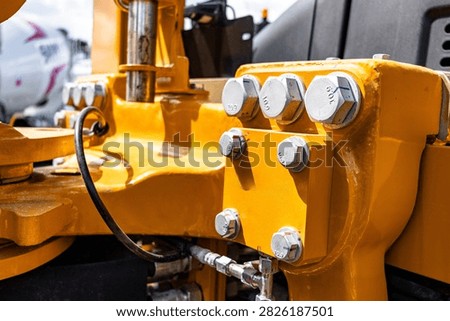Wheel loader yellow frame chassis heavy steel bolt joint connection. Modern construction machinery component with high strength fasteners row and transport vehicle engineering technical details.