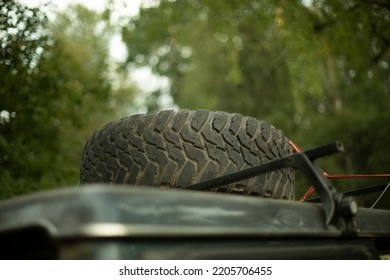 Wheel On Roof Of Car. Spare Tire On Trunk. Transport For Forests. Tire With Deep Tread.