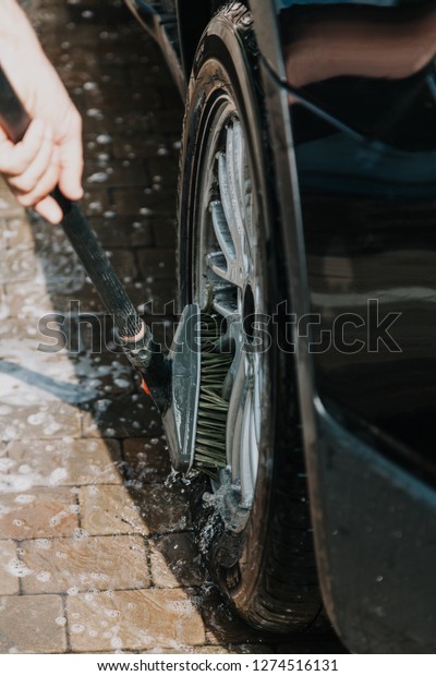 Wheel wash of a black car wheel with a special\
brush on a long handle\
