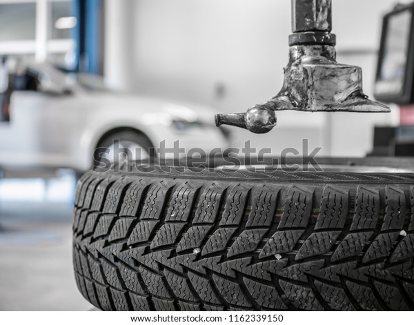 Wheel\
whit winter tire on tire changing machine in a workshop. Wheel on\
tire changing machine. White car in background.\
