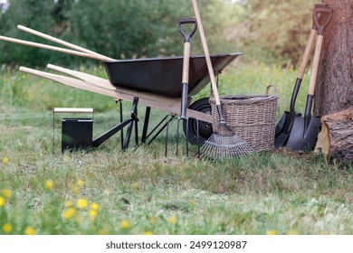 A wheelbarrow and gardening tools in the natural environment of fields and meadows. Autumn work in the garden.