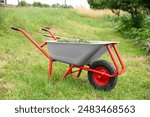 Wheelbarrow with mown grass and pitchfork outdoors