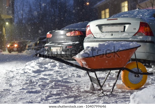 wheelbarrow\
with snow on parking cars in yard in\
blizzard